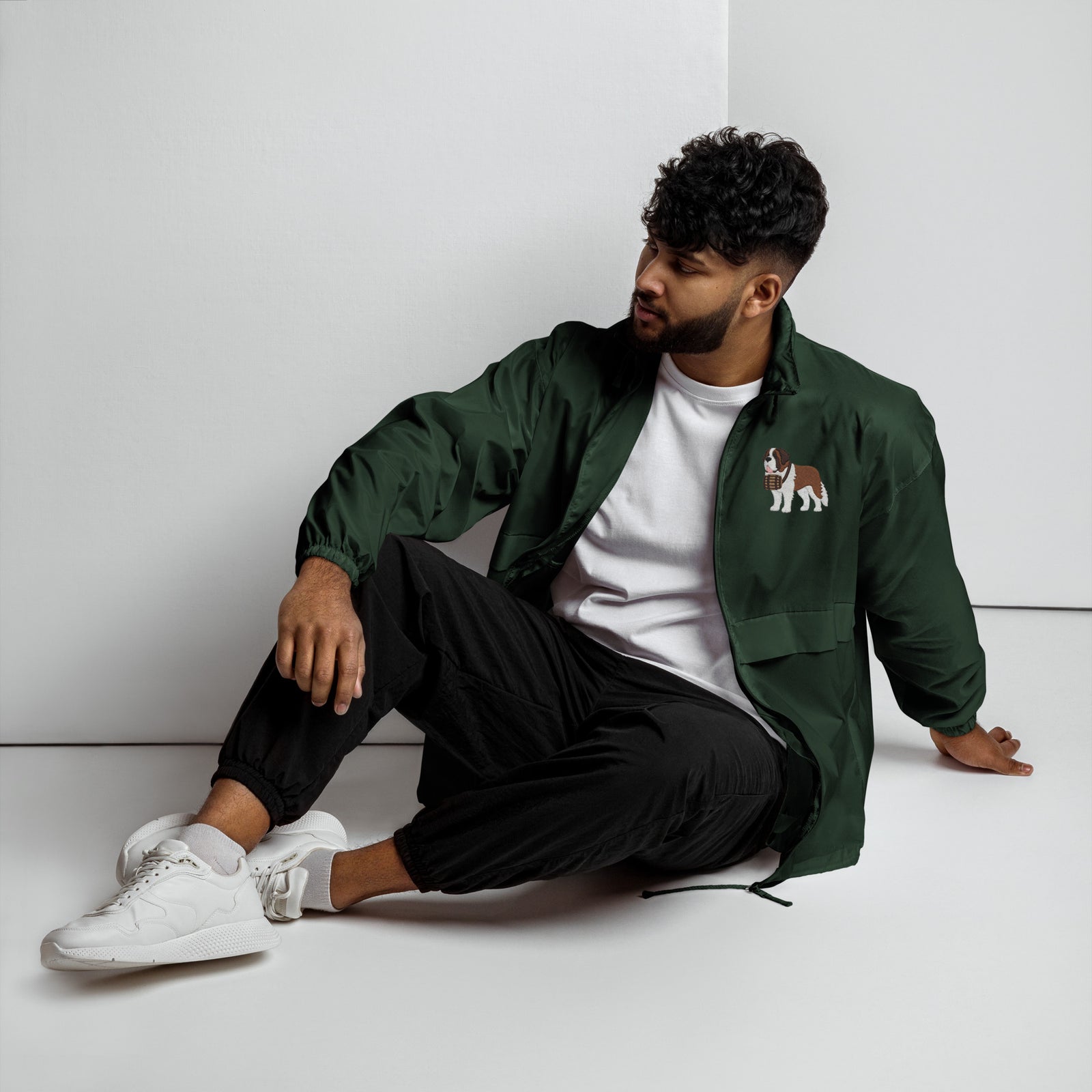 Lightweight, packable forest green windbreaker with chest embroidered Saint Bernard and barrel, adjustable hood, elastic cuffs, and zip pockets.