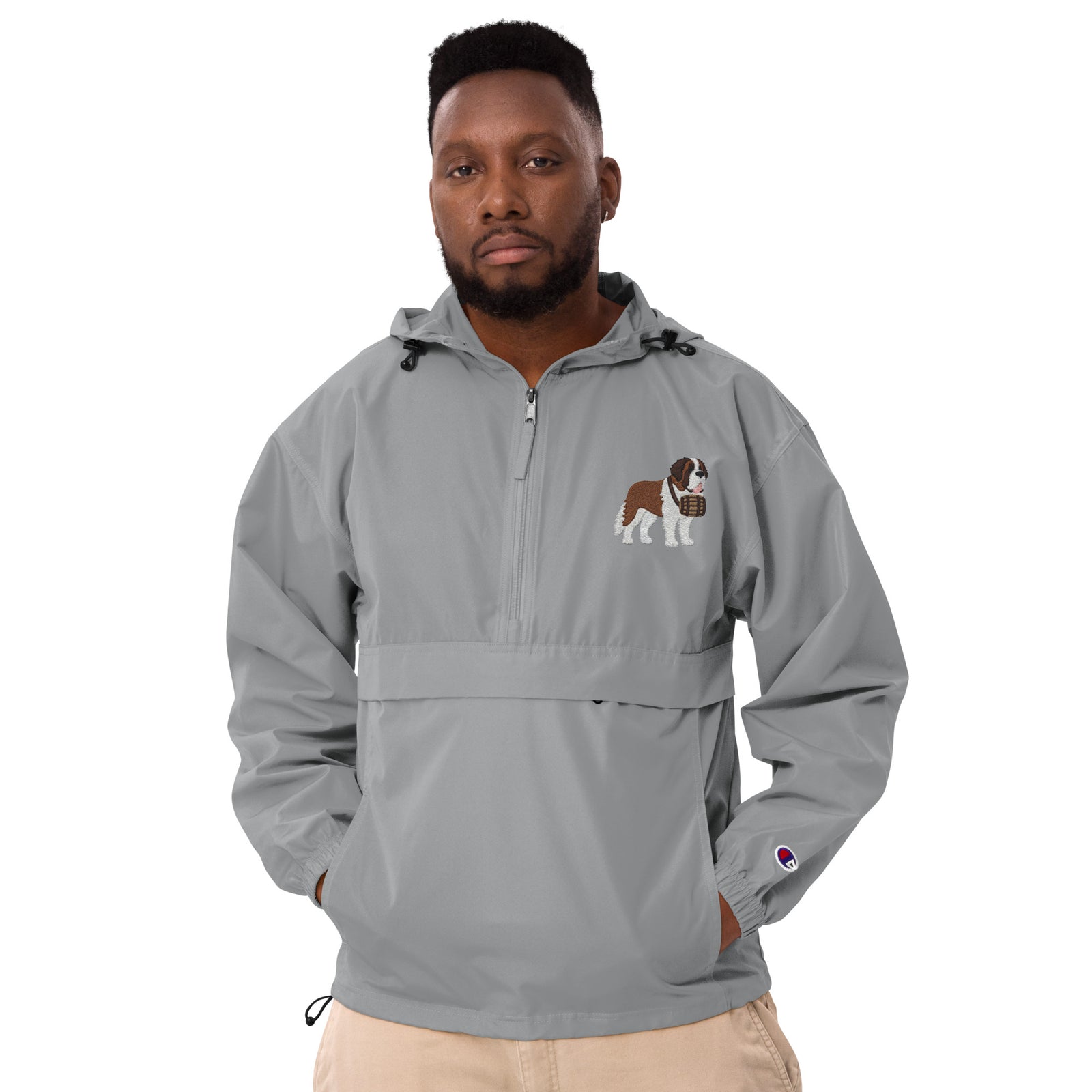 Light gray Champion packable windbreaker with chest embroidered Saint Bernard and barrel, half zip pullover with hood, kangaroo pocket, and zip pouch.