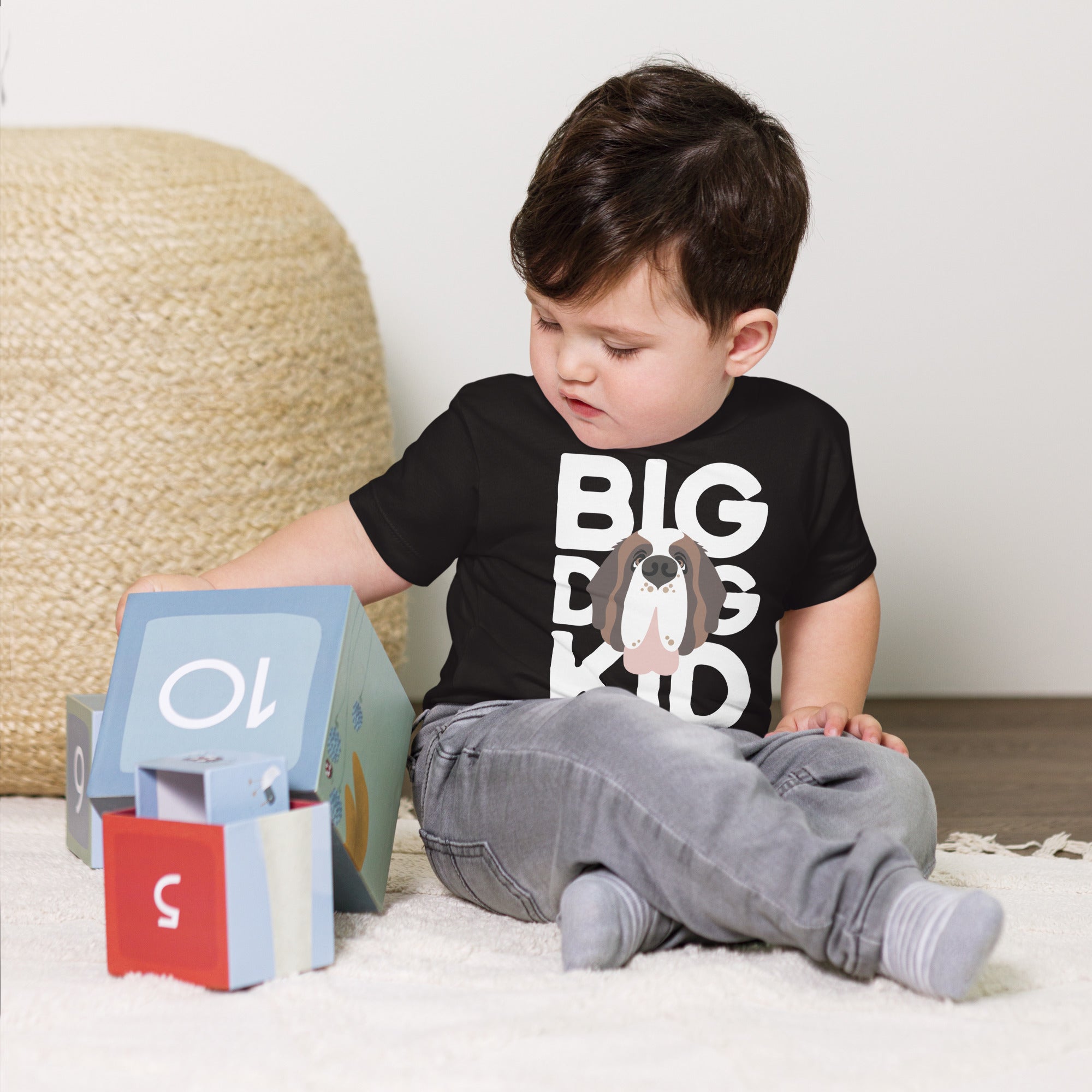 Child wearing a black t-shirt with 'BIG DOG KID' text and a Saint Bernard dog graphic, playing with colorful blocks on a light-colored rug.