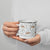 Lightweight 12 oz enamel camp mug. Features a modern pattern of Saint Bernard dogs, mountains and pine trees on a white background by Lucy and Norman