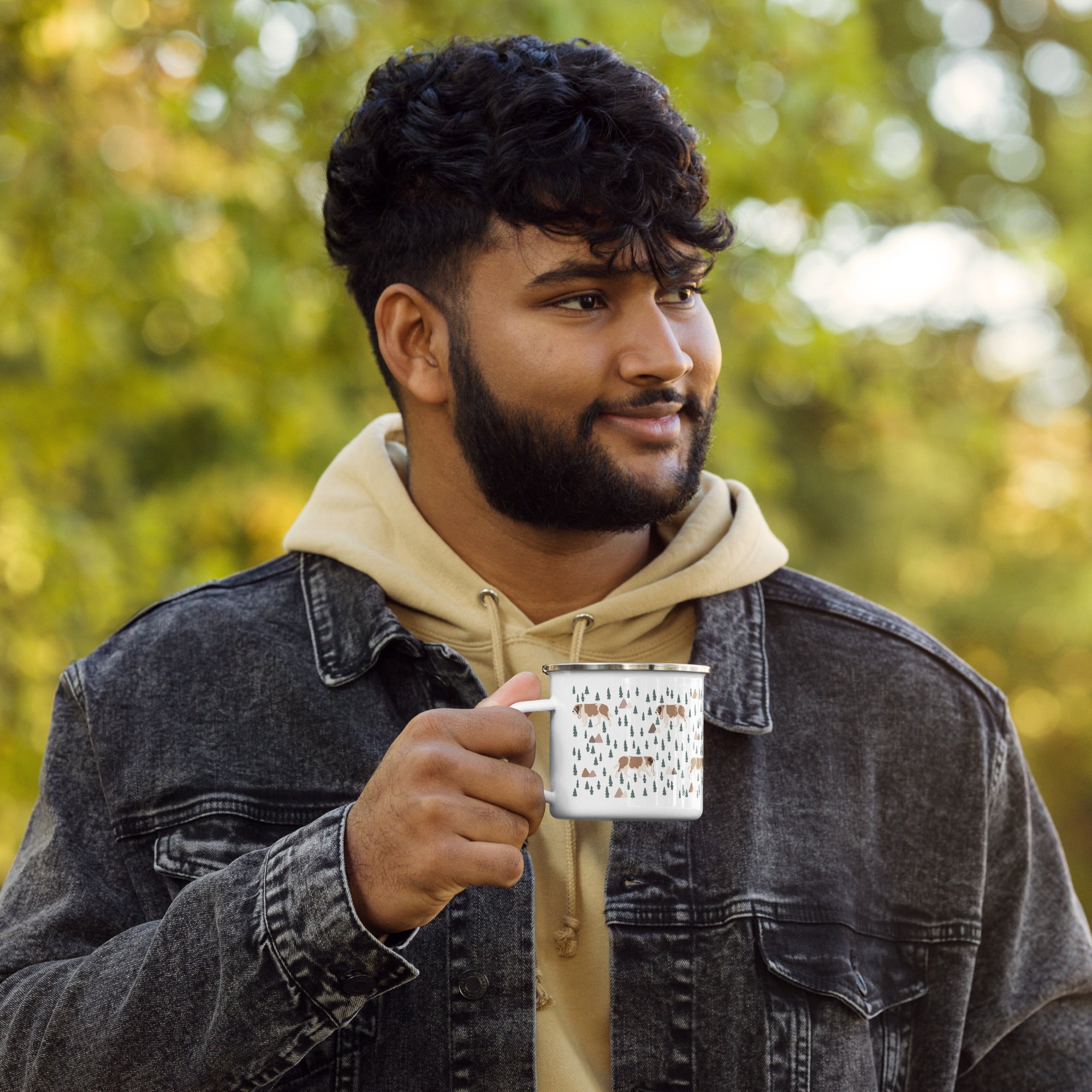 Man holding lightweight 12 oz enamel camp mug. Features a modern pattern of Saint Bernard dogs, mountains and pine trees on a white background by Lucy and Norman