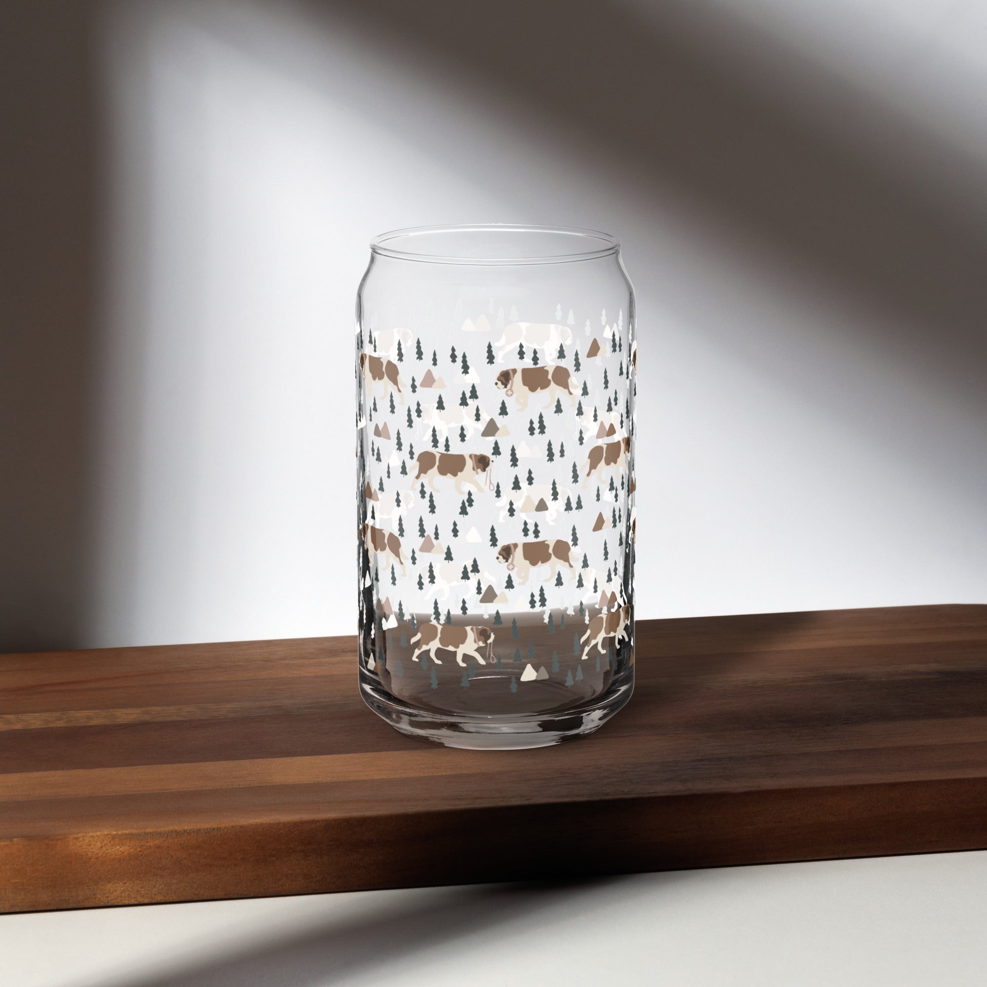 16 oz can-shaped glass tumbler. Features a modern pattern of Saint Bernard dogs, mountains and pine trees by Lucy and Norman