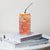 16 oz can-shaped glass tumbler, bamboo wood lid and metal straw. Features a modern pattern of Saint Bernard dogs, mountains and pine trees by Lucy and Norman