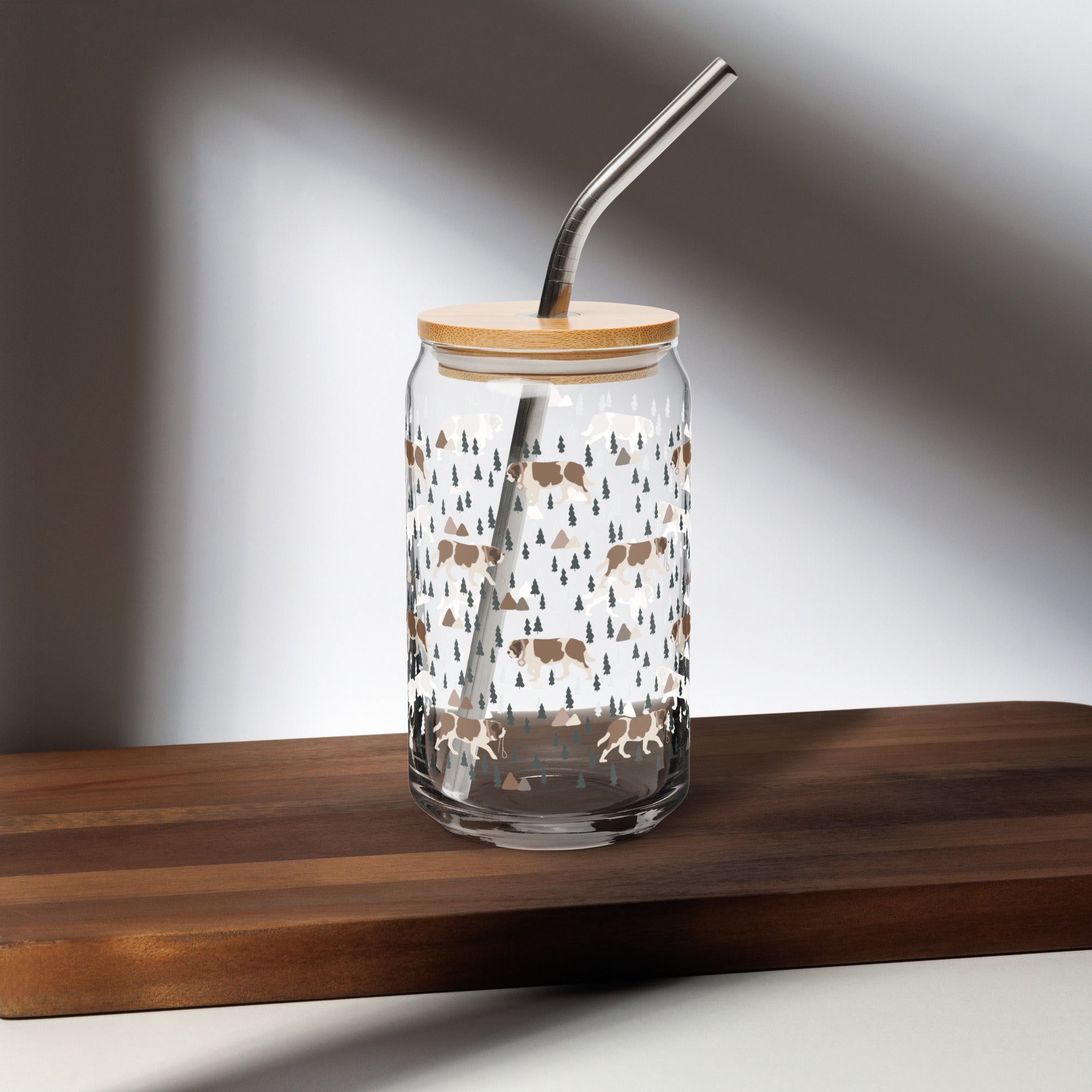 16 oz can-shaped glass tumbler, bamboo wood lid and metal straw. Features a modern pattern of Saint Bernard dogs, mountains and pine trees by Lucy and Norman