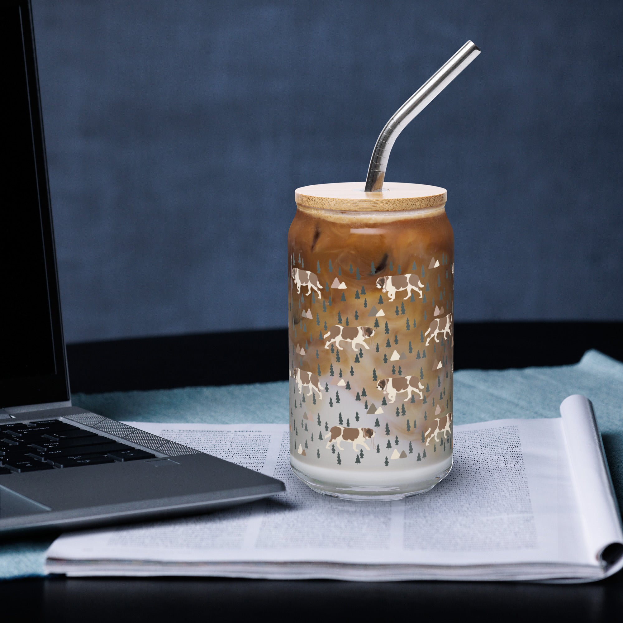 16 oz can-shaped glass tumbler, bamboo wood lid and metal straw. Features a modern pattern of Saint Bernard dogs, mountains and pine trees by Lucy and Norman