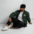 Lightweight, packable forest green windbreaker with chest embroidered Saint Bernard and barrel, adjustable hood, elastic cuffs, and zip pockets.