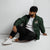 Lightweight, packable forest green windbreaker with chest embroidered Saint Bernard and barrel, adjustable hood, elastic cuffs, and zip pockets.