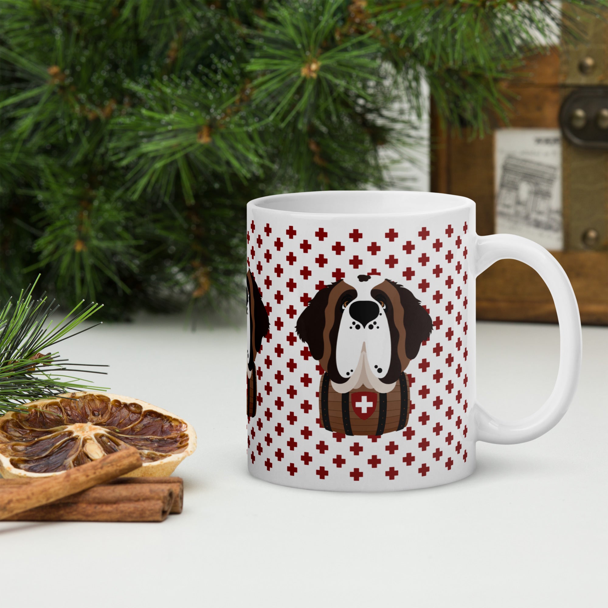 White ceramic 11 ounce mug featuring a cute illustrated Saint Bernard dog wearing a rescue barrel, surrounded by a red Swiss cross pattern. Perfect gift for St Bernard dog lovers and Swiss Alps fans by Lucy and Norman.