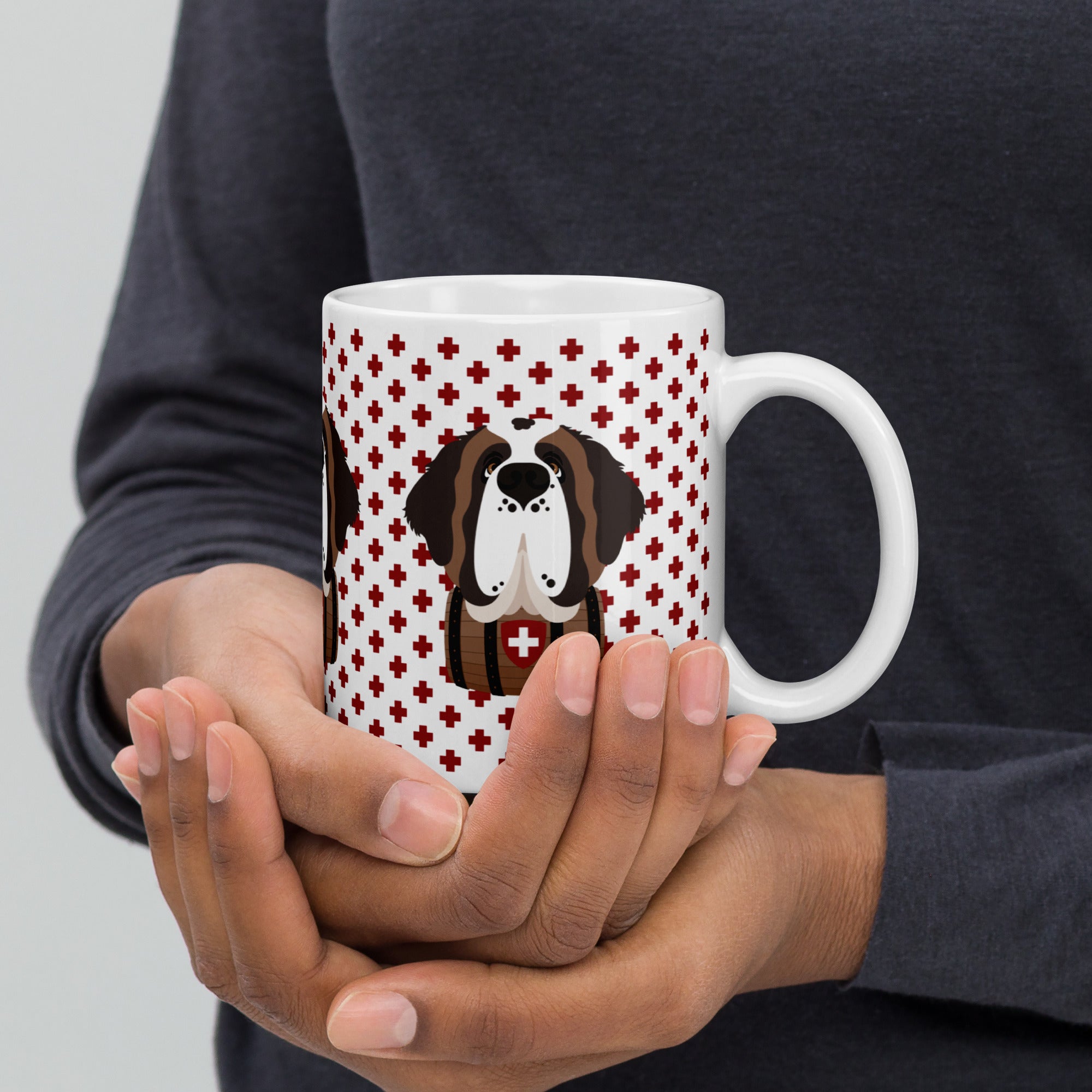 White ceramic mug featuring a cute illustrated Saint Bernard dog wearing a rescue barrel, surrounded by a red Swiss cross pattern. Perfect gift for St Bernard dog lovers and Swiss Alps fans by Lucy and Norman.