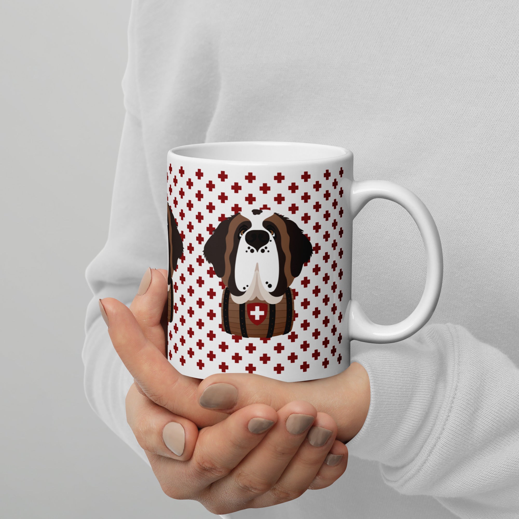 White ceramic mug featuring a cute illustrated Saint Bernard dog wearing a rescue barrel, surrounded by a red Swiss cross pattern. Perfect gift for St Bernard dog lovers and Swiss Alps fans by Lucy and Norman.