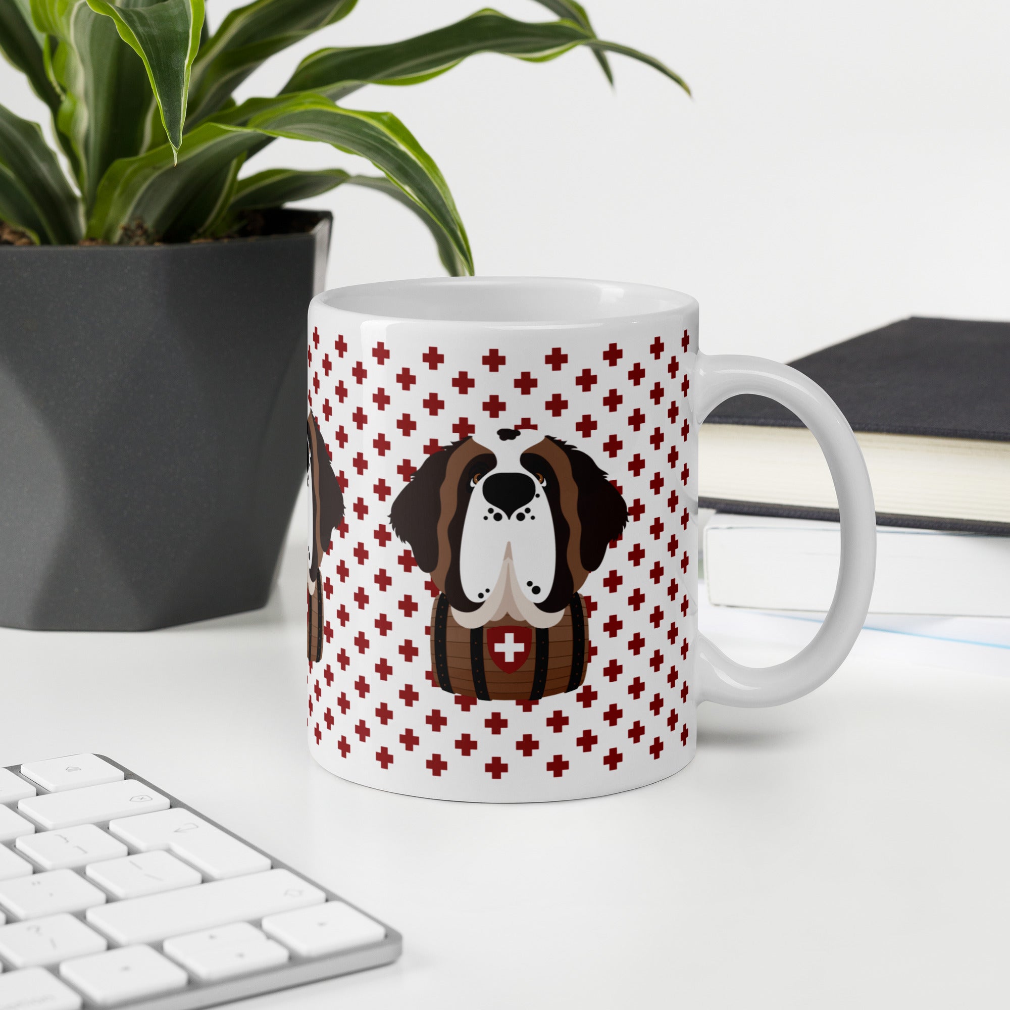 White ceramic mug featuring a cute illustrated Saint Bernard dog wearing a rescue barrel, surrounded by a red Swiss cross pattern. Perfect gift for St Bernard dog lovers and Swiss Alps fans by Lucy and Norman.
