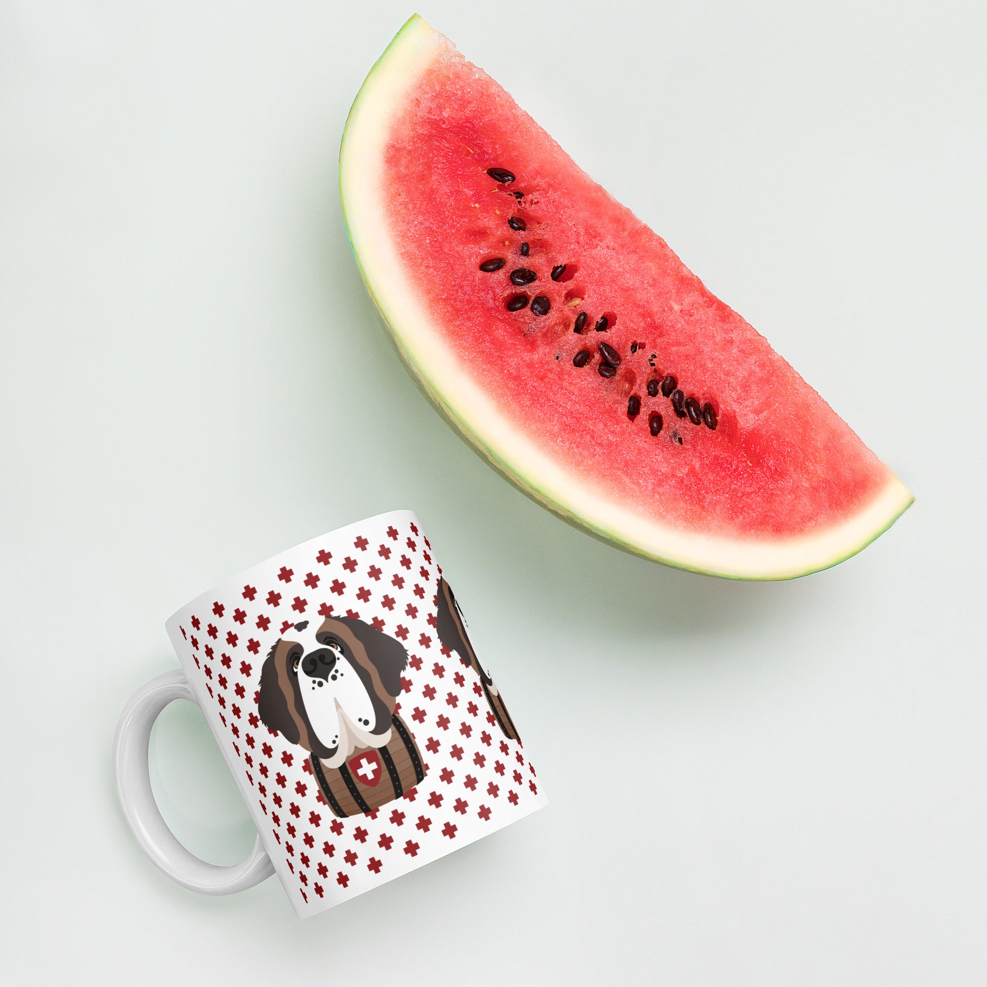 White ceramic 11 ounce mug featuring a cute illustrated Saint Bernard dog wearing a rescue barrel, surrounded by a red Swiss cross pattern. Perfect gift for St Bernard dog lovers and Swiss Alps fans by Lucy and Norman.