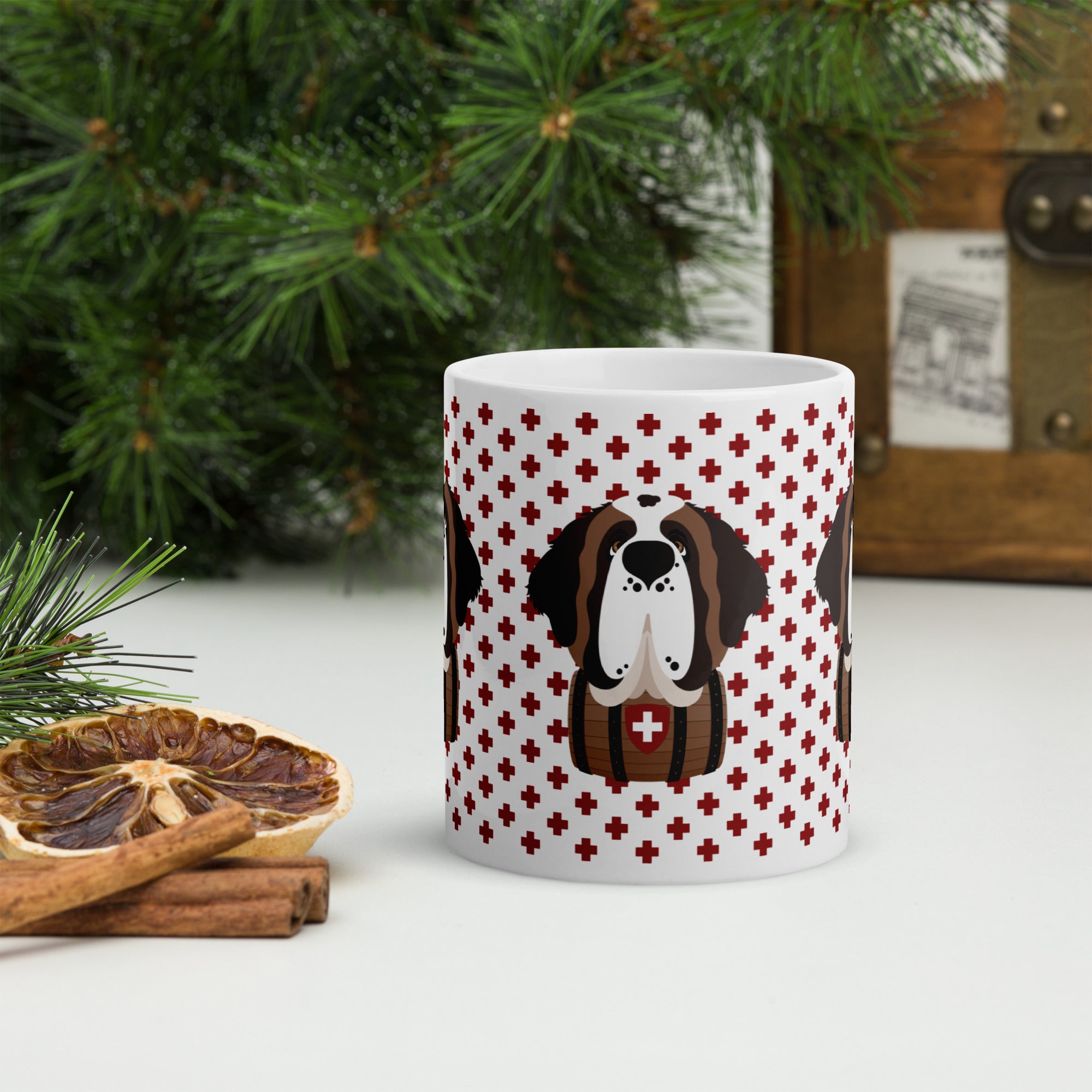 White ceramic 11 ounce mug featuring a cute illustrated Saint Bernard dog wearing a rescue barrel, surrounded by a red Swiss cross pattern. Perfect gift for St Bernard dog lovers and Swiss Alps fans by Lucy and Norman.