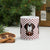 White ceramic 11 ounce mug featuring a cute illustrated Saint Bernard dog wearing a rescue barrel, surrounded by a red Swiss cross pattern. Perfect gift for St Bernard dog lovers and Swiss Alps fans by Lucy and Norman.
