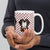 White ceramic 15 ounce mug featuring a cute illustrated Saint Bernard dog wearing a rescue barrel, surrounded by a red Swiss cross pattern. Perfect gift for St Bernard dog lovers and Swiss Alps fans by Lucy and Norman.
