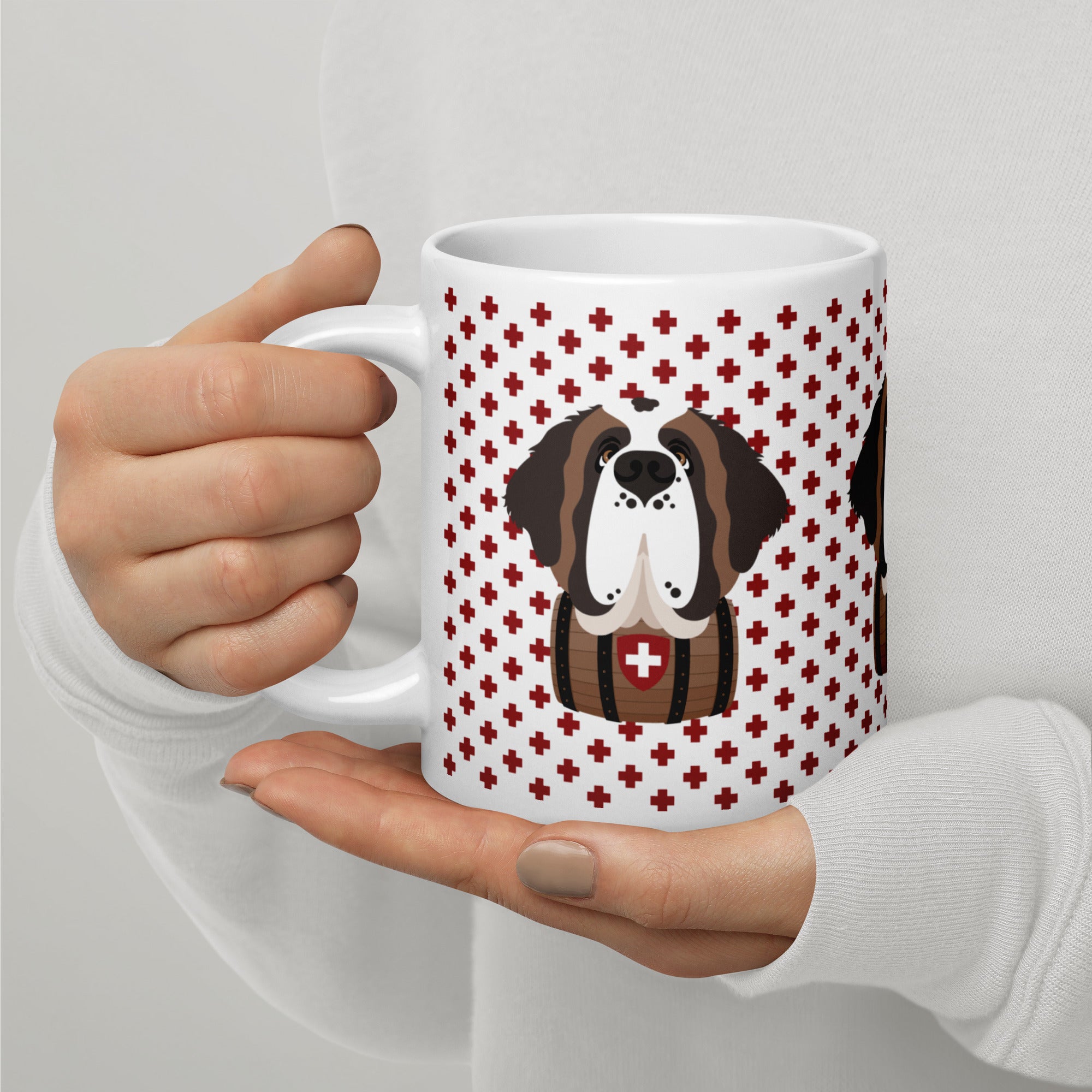 White ceramic 20 ounce mug featuring a cute illustrated Saint Bernard dog wearing a rescue barrel, surrounded by a red Swiss cross pattern. Perfect gift for St Bernard dog lovers and Swiss Alps fans by Lucy and Norman.