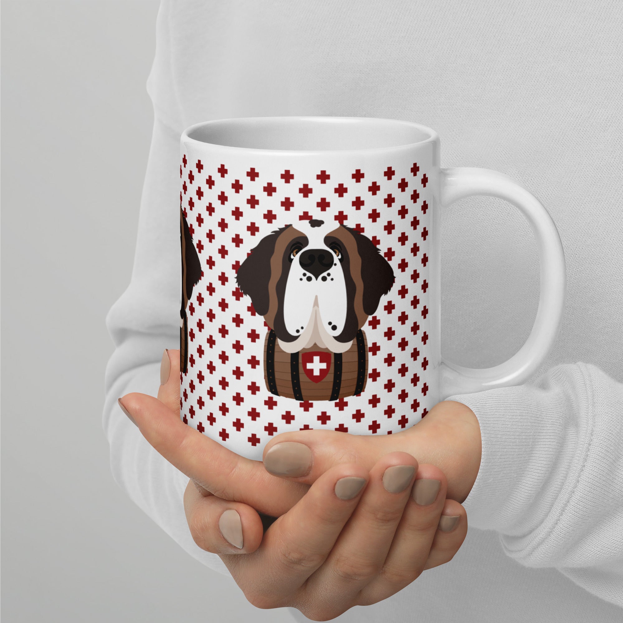 White ceramic 20 ounce mug featuring a cute illustrated Saint Bernard dog wearing a rescue barrel, surrounded by a red Swiss cross pattern. Perfect gift for St Bernard dog lovers and Swiss Alps fans by Lucy and Norman.