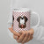 White ceramic 20 ounce mug featuring a cute illustrated Saint Bernard dog wearing a rescue barrel, surrounded by a red Swiss cross pattern. Perfect gift for St Bernard dog lovers and Swiss Alps fans by Lucy and Norman.